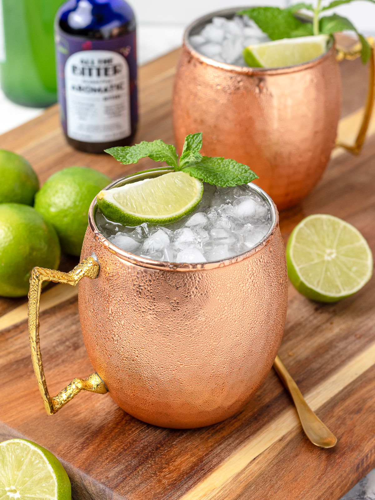 Moscow Mule Mocktails in copper mugs chilled with tons of ice, and lime wedges and mint leaves. bitters on the side.