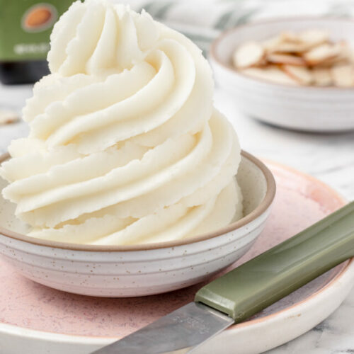 Large swirl of frosting in a dish. Slivered almonds and almond extract surround it.