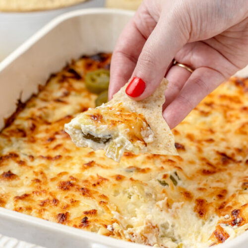 Hand holding a chip loaded with Jalapeno Artichoke Dip.