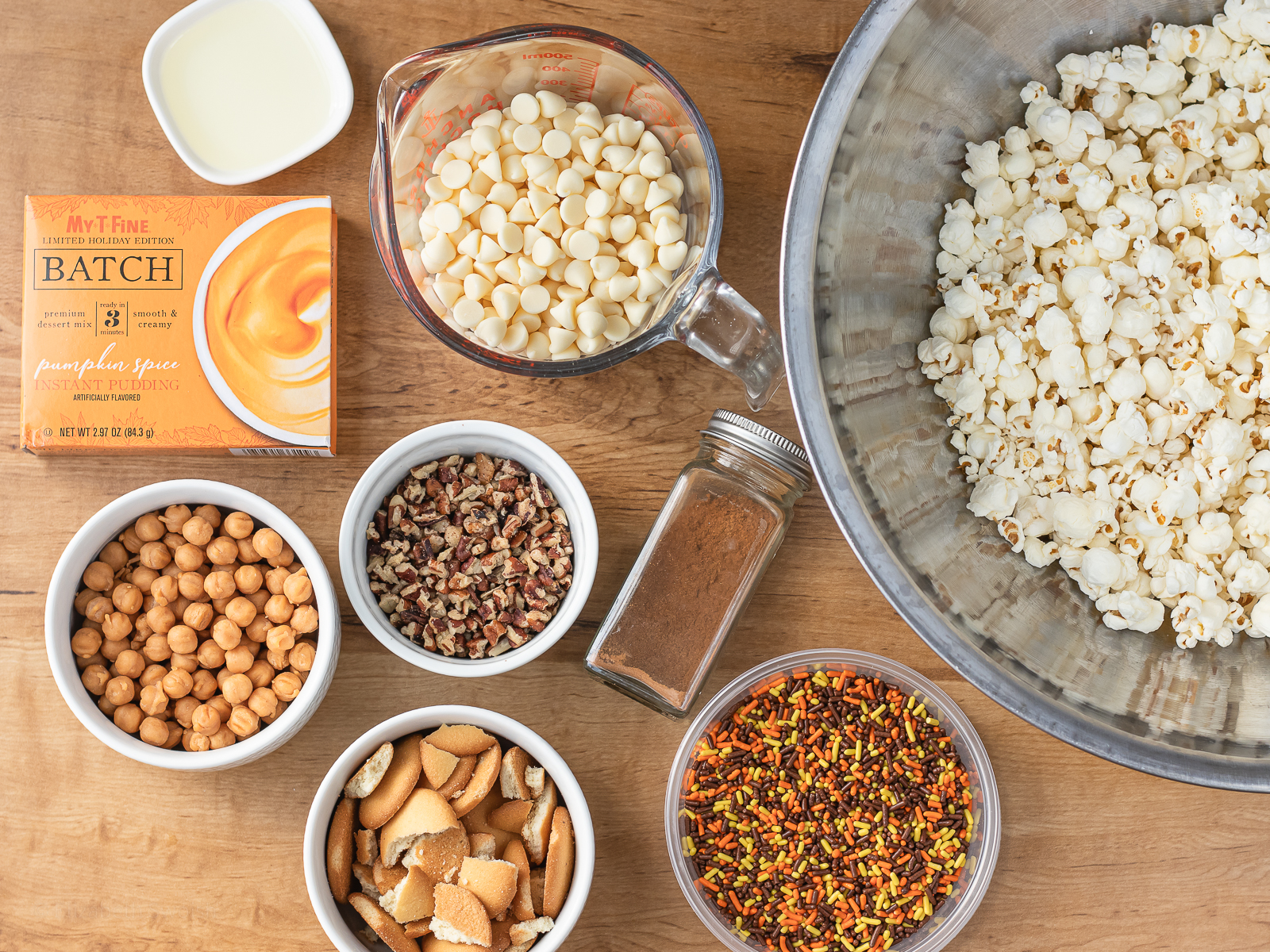 Ingredients needed. Plain popcorn, melted white chocolate, pumpkin spice pudding, cinnamon, caramel bits, chopped toasted pecans, vanilla wafer cookies and festive fall sprinkles.