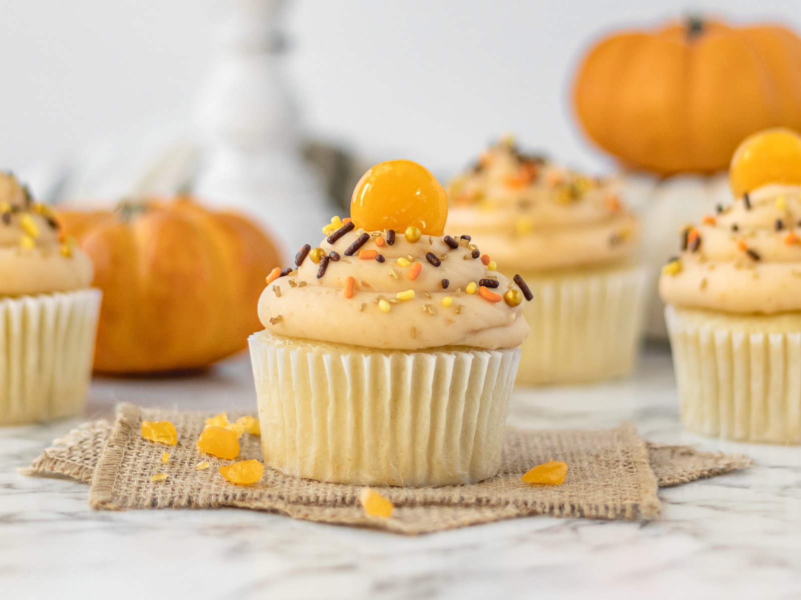 Close up of vanilla cupcake filled with butterscotch pudding and topped with a butterscotch buttercream, fall sprinkles, and a butterscotch candy.