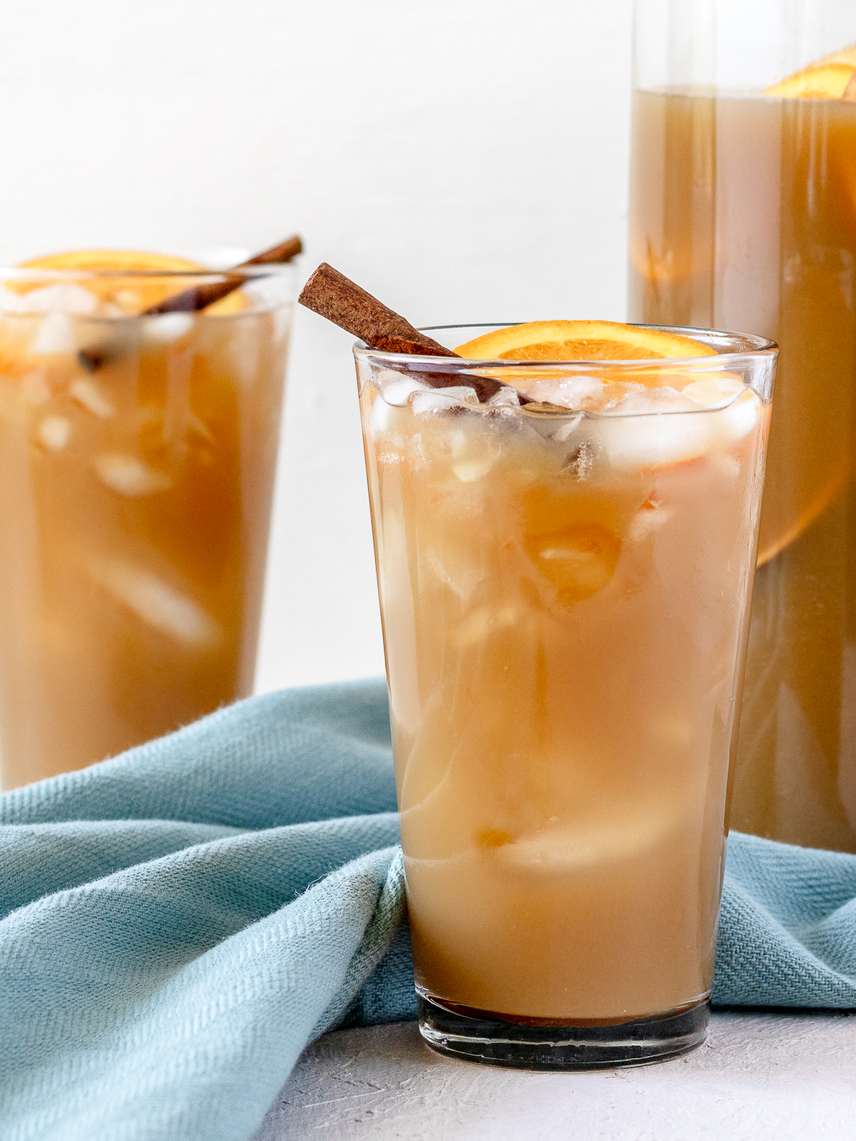 Glasses of ice filled with non alcoholic sweet tea harvest punch. Garnished with an orange slice and cinnamon stick.
