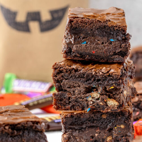 Stack of brownies surrounded by leftover Halloween candy and a treat bag in the background.