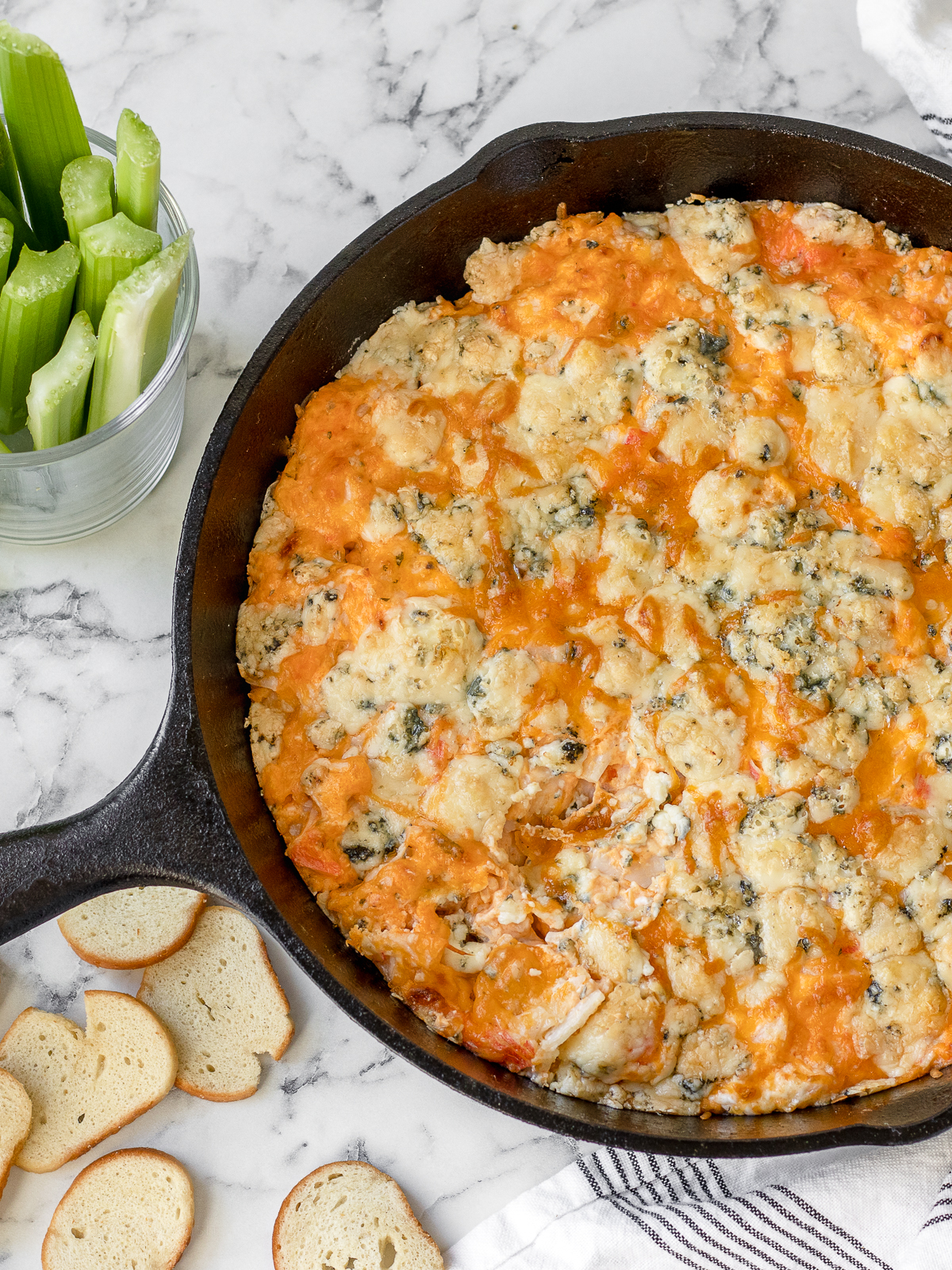 Steaming hot Buffalo Crab Dip in a cast iron skillet surrounded by bagel chips and celery.