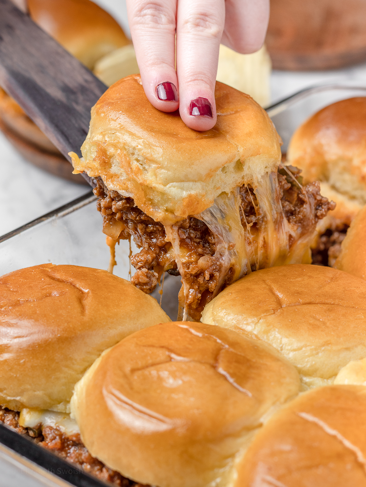 Pulling a slider out of the pan to see cheese pull and tons of Sloppy Joe filling.