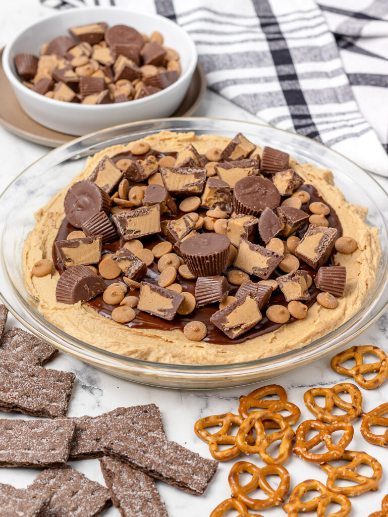 Layer 3 of dip, peanut butter chips and peanut butter cups. Surrounded by pretzels and chocolate graham cracker.
