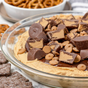 Dish filled with Chocolate Peanut Butter Pie Dip and topped with lots of peanut butter chips and peanut butter cups. Chocolate graham crackers and pretzels on the side for dipping.