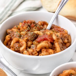 A bowl of meaty Venison Goulash with dinner rolls served on the side.