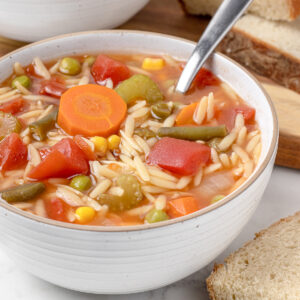 A bowl of Vegetable Orzo Soup ready to eat with bread.