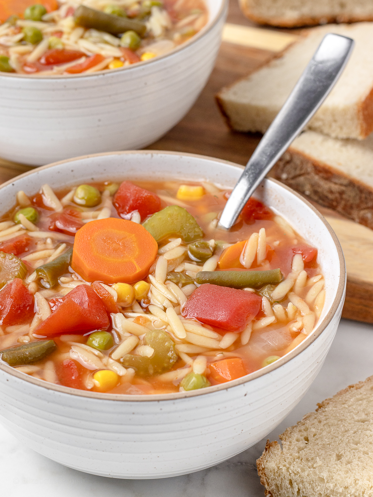 Close up of soup to see carrots, corn, peas, green beans, tomatoes, celery, onion, and orzo pasta.