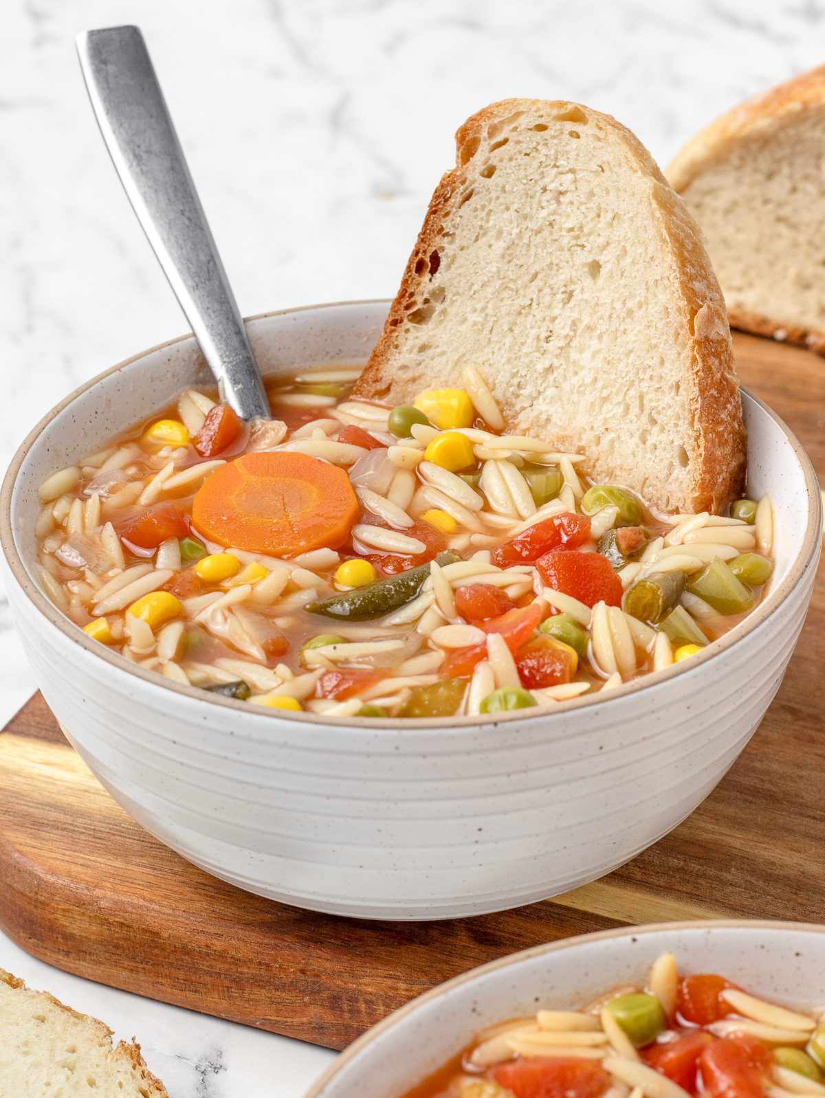 Vegetable Orzo Soup with a slice of crusty bread in it, ready to eat.