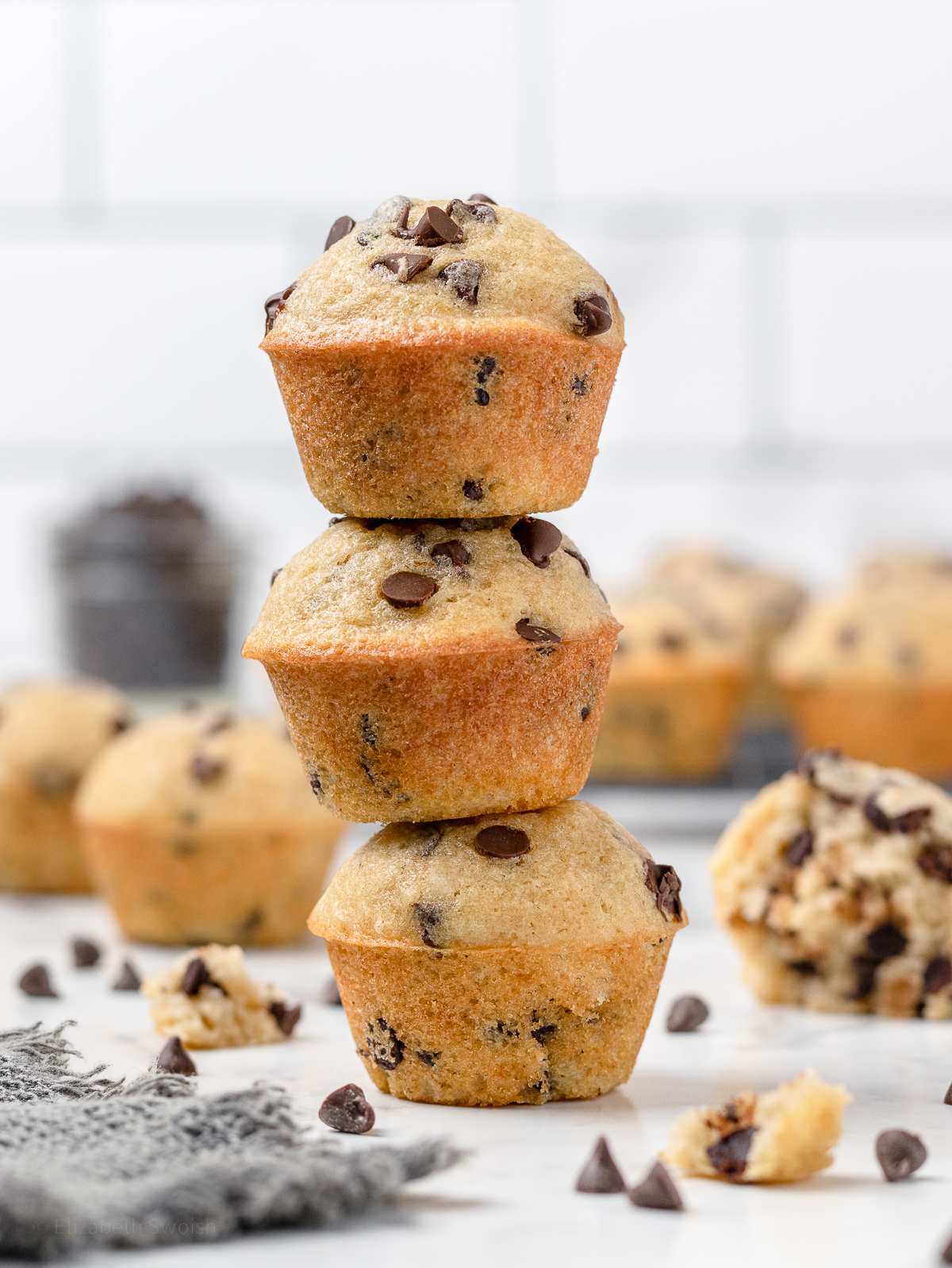 Stack of 3 mini muffins surrounded by more muffins and mini semi-sweet chocolate chips.