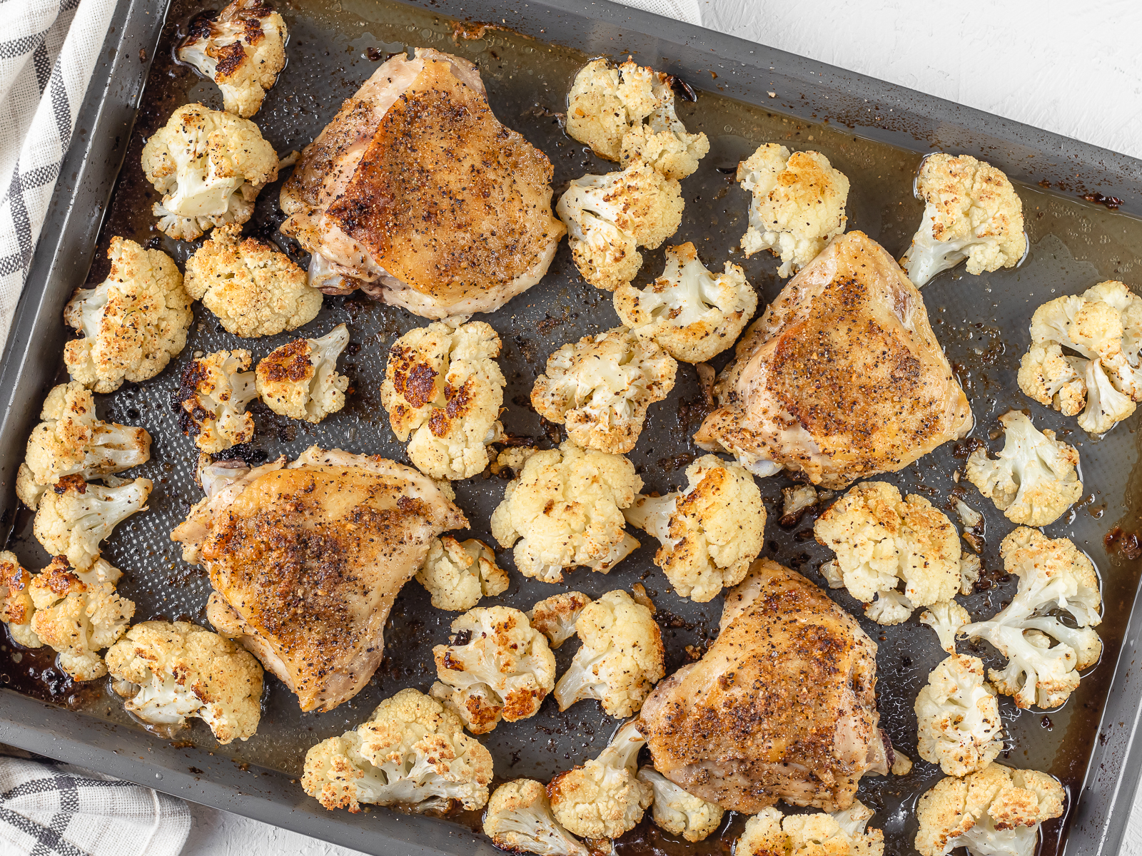 A baking sheet with baked Cajun Chicken Thighs and roasted cauliflower.