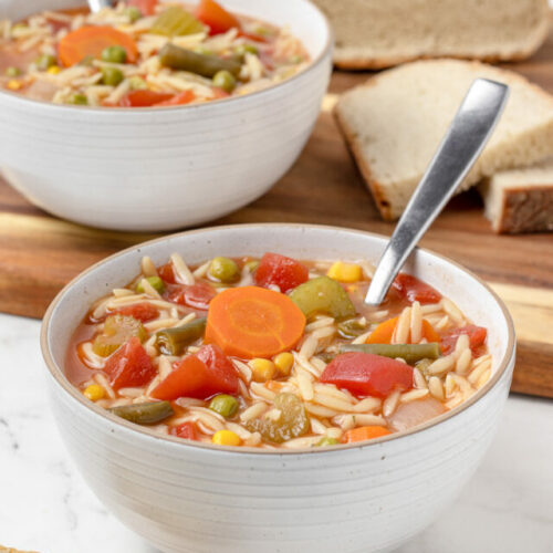 Two bowls of soup loaded with vegetables and small orzo pasta served with Artisan bread.