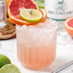 An iced Paloma Mocktail with a salted rim, lime and grapefruit slices.