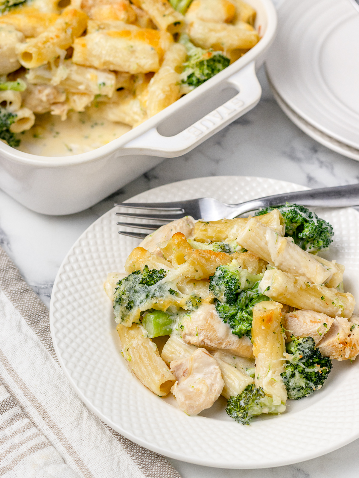 Baked Chicken and Broccoli Pasta on a plate and more in a large baking dish.