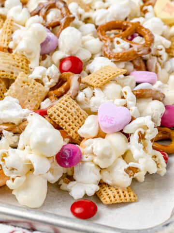 Valentines Day Popcorn with mini pretzels and corn squares cereal, coated with marshmallow, and topped with M&M's and conversation hearts.