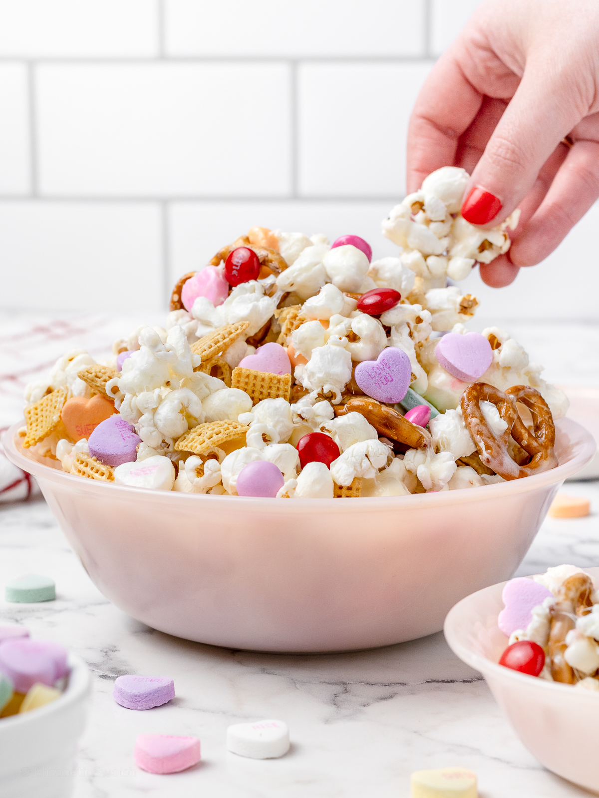 Hand grabbing the marshmallow coated popcorn snack mix out of a pink bowl