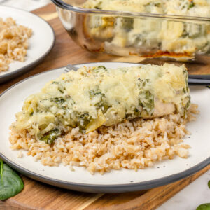 A plate of Spinach Artichoke Chicken Bake and rice, ready to cut and eat.