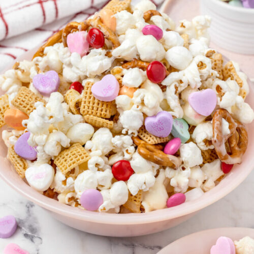 A bowl filled with popcorn snack mix. You see conversation hearts, M&M's and gooey marshmallow throughout.