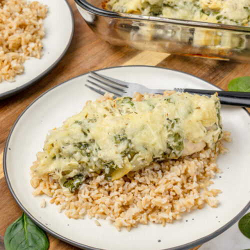 Spinach Artichoke Chicken on top of a bed of brown rice, served on a plate with a fork ready to eat.