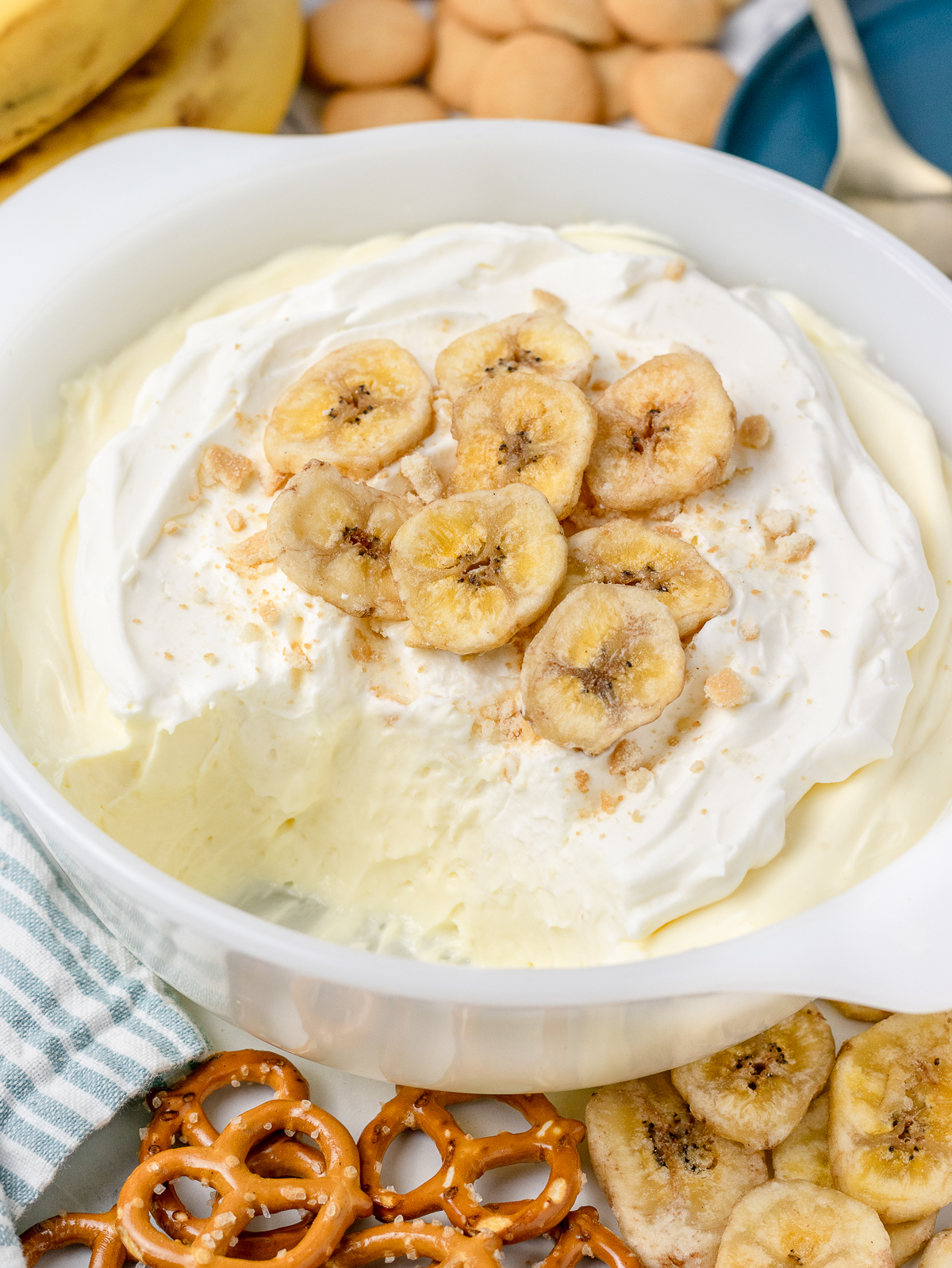A big scoop of dip taken out of the dish to reveal layers of banana cream pie and whipped cream that is topped with crushed vanilla wafers, and banana chips.
