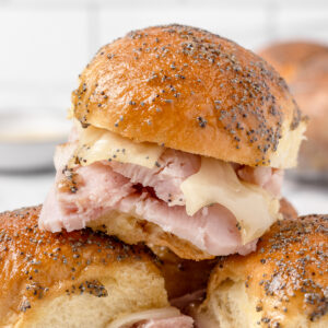 Stack of 3 Brown Sugar Ham and Cheese Sliders on a plate with more in the background.