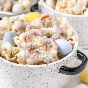 Bunny Popcorn Snack Mix with white chocolate coated popcorn, pretzels, toasted O's cereal topped with milk chocolate candy eggs, and pastel Easter sprinkles.