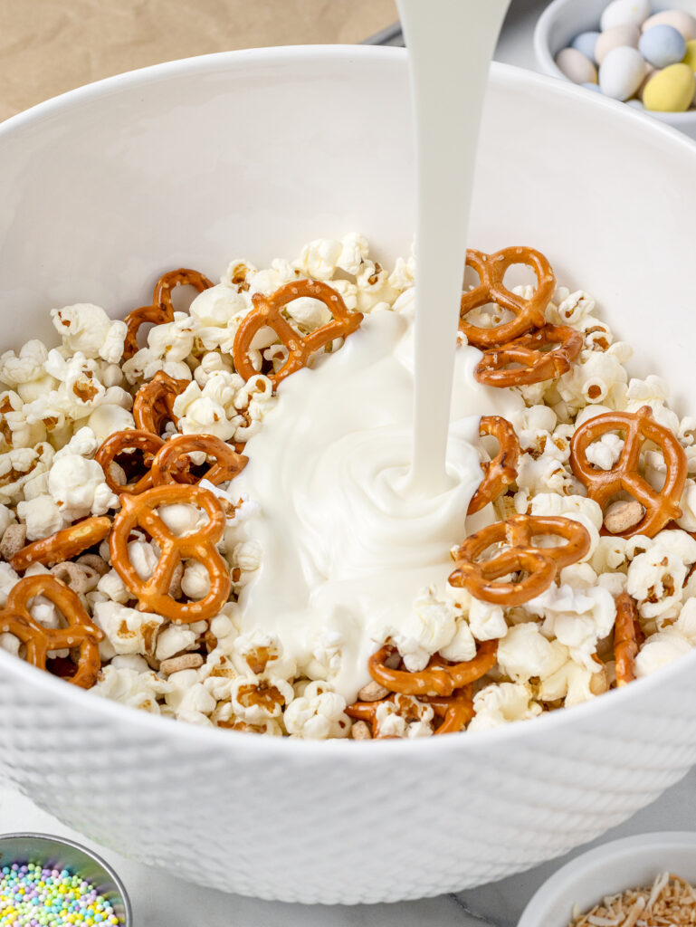 Pouring melted white chocolate over the popcorn snack mix.