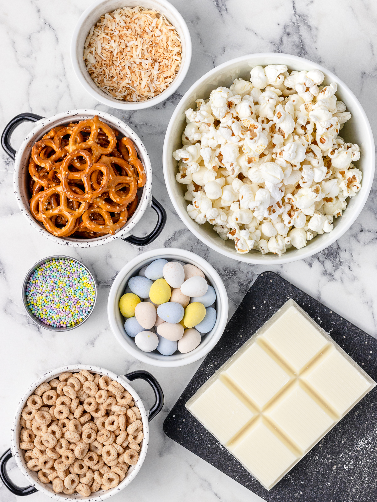 Ingredients. Plain popcorn, mini pretzels, toasted O's cereal, toasted unsweetened coconut, white chocolate or almond bark, milk chocolate eggs, and pastel Easter sprinkles.