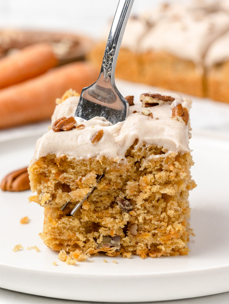 A hand holding a fork that is digging into the Carrot Snack Cake.
