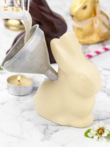 3. Pouring the mocktail from a shaker bottle into a small funnel until the chocolate bunny is filled.