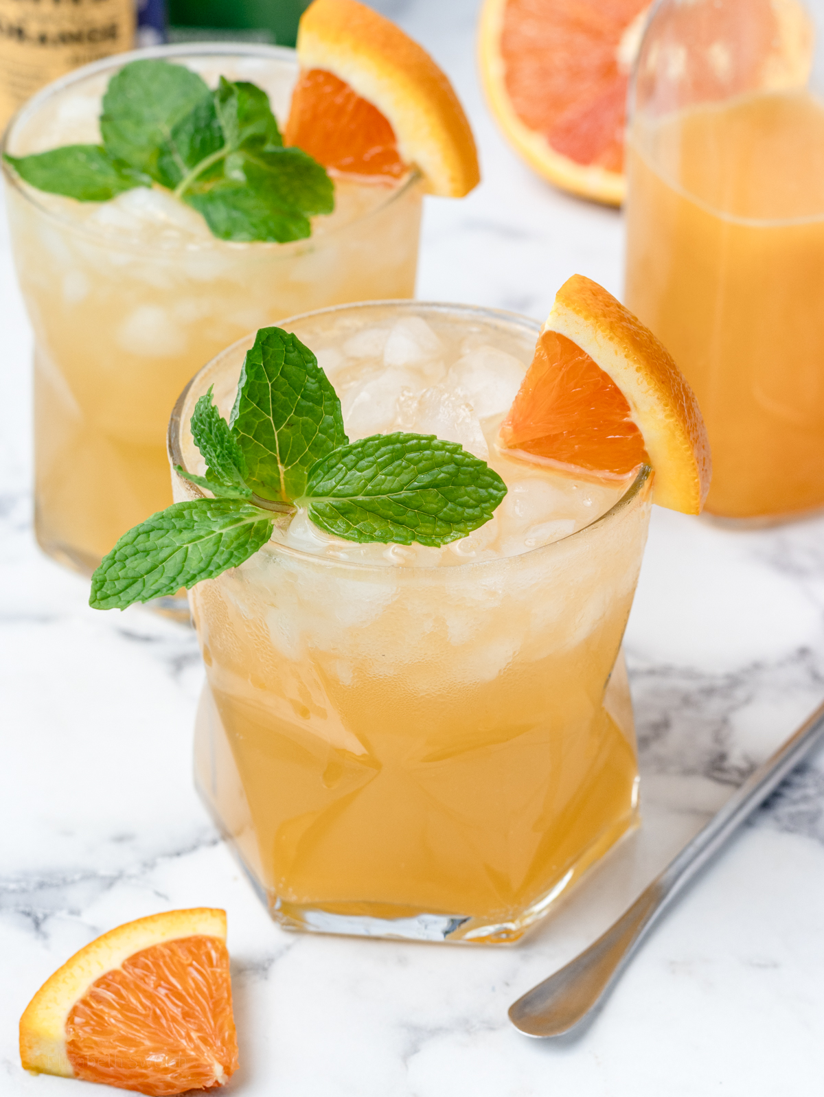 2 glasses of orange coconut water mocktail garnished with mint leaves and orange wedges.