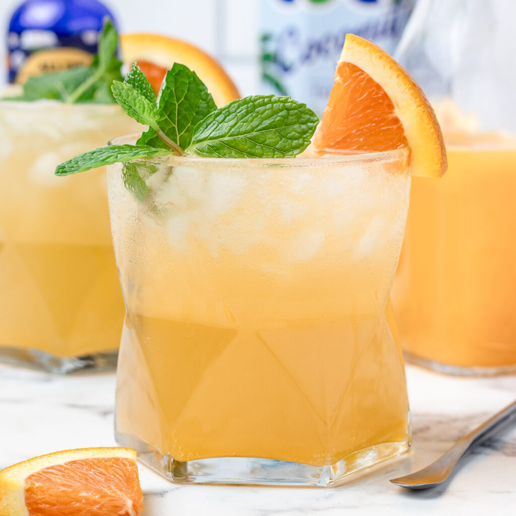 An iced Orange Coconut Water Mocktail with fresh mint and orange slices. They are a light and refreshing orange color.