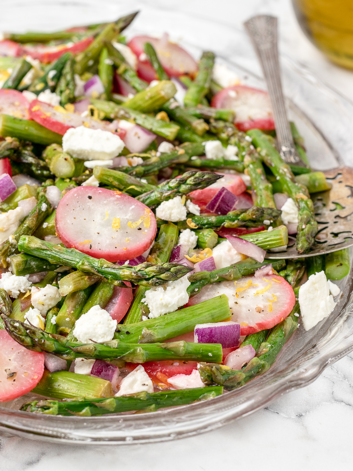 Close up of radish and asparagus salad to see flecks of black pepper and lemon zest with chunks of feta cheese