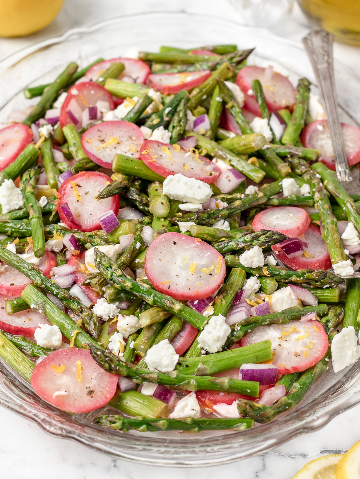 Platter of roasted radishes and asparagus topped with red onion, and feta cheese tossed in lemon juice and lemon zest.