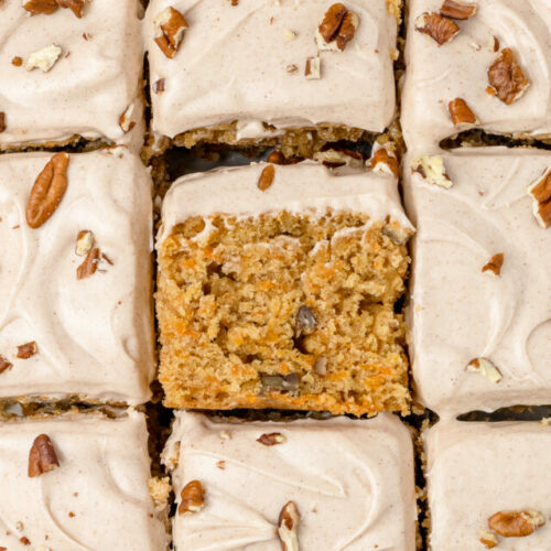 On overhead view of the Carrot Snack Cake cut into 9 pieces. The center slice is flipped on its side to see the interior of the cake.