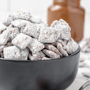 Bowl of Nutella Puppy Chow coated in hazelnut spread, chocolate, and powdered sugar.