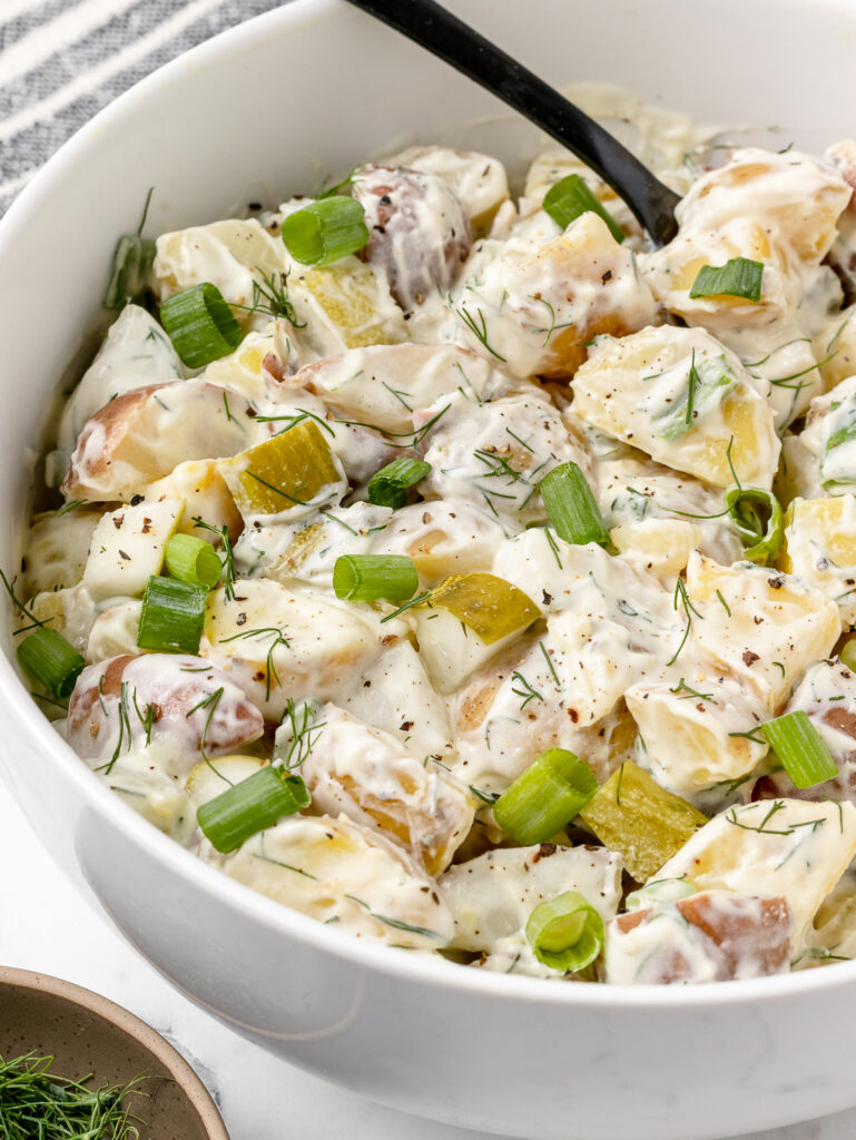 Close up of the Potato Salad to see the creamy dressing, tender potatoes, dill pickles, and herbs on top.