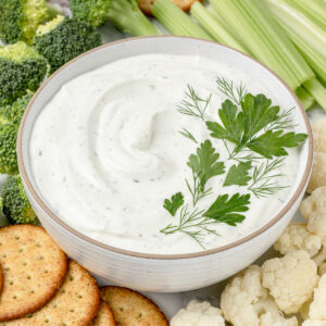 Bowl of Cottage Cheese Ranch Dip topped with fresh parsley and fresh dill. There is vegetables and crackers on the side for dipping.