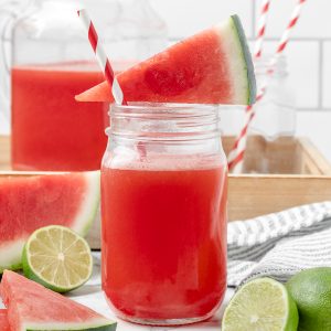 Jar of Watermelon Limeade with a watermelon slice sitting on top and a red and white striped straw.