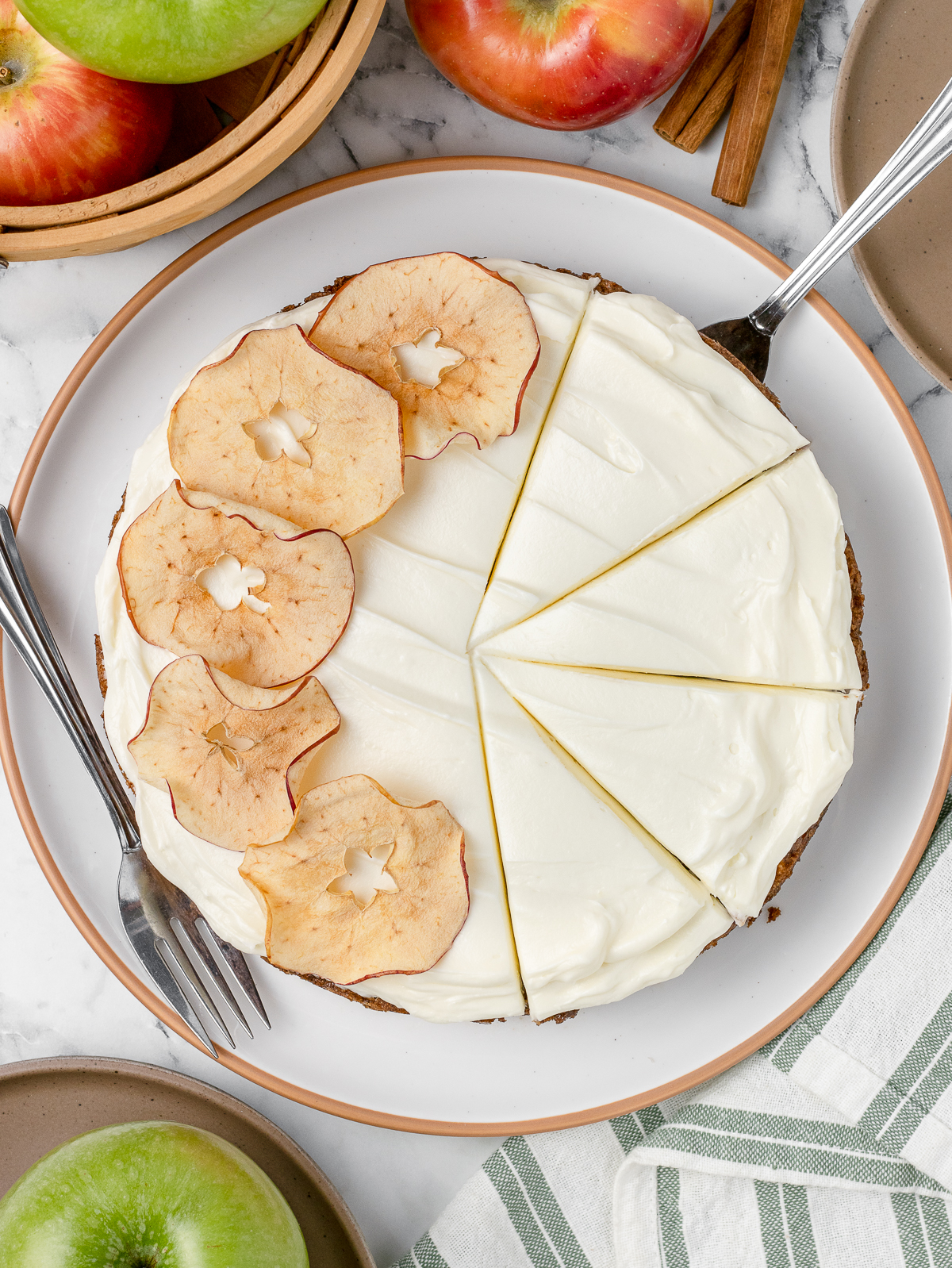 Overhead image of the Apple Spice Cake with 4 slices cut. There is a cream cheese frosting and curve of dried apple slices to the left.