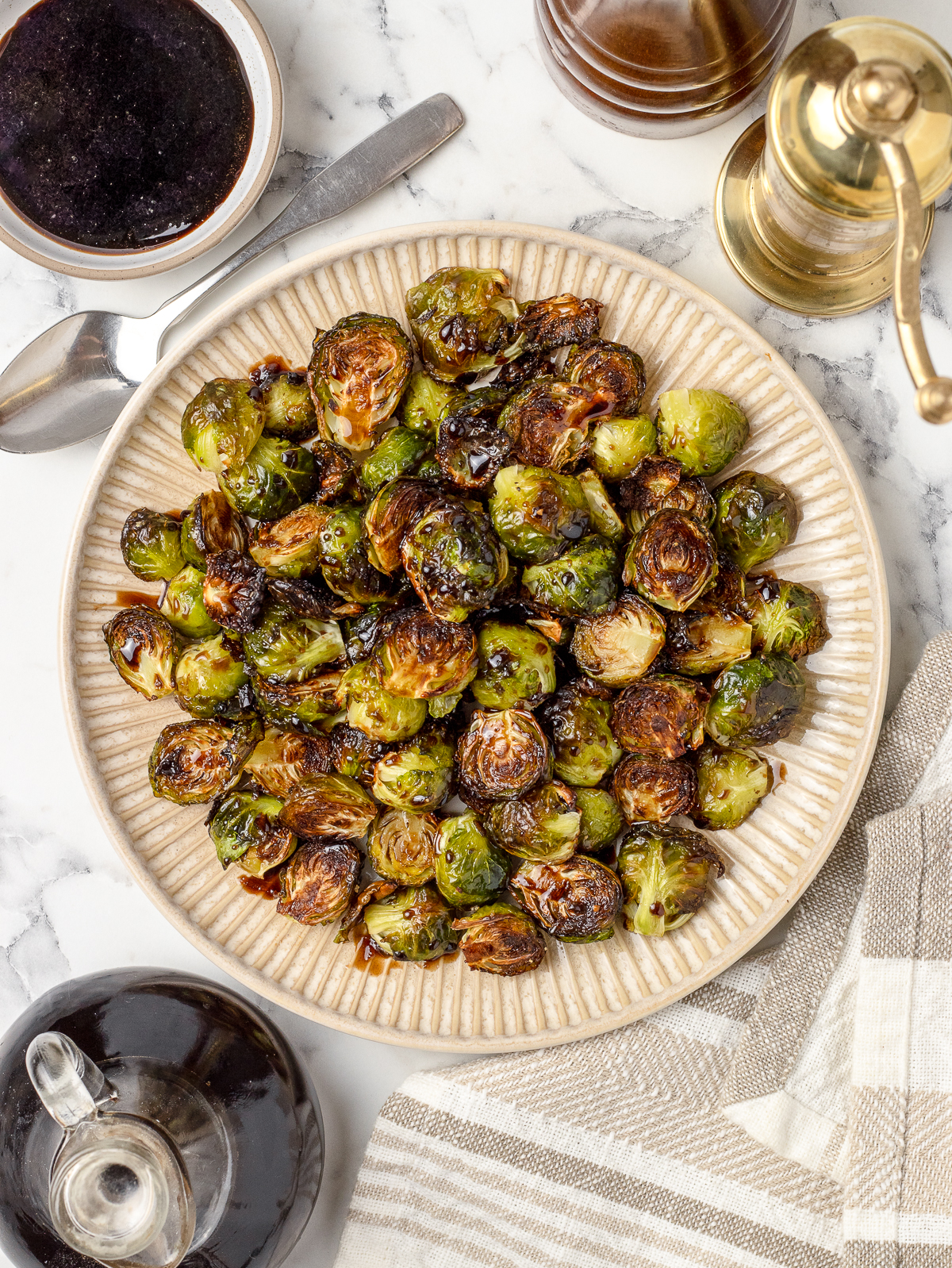 A large platter filled with roasted brussels sprouts. They are glazed in a balsamic honey sauce and there is more on the side for dipping.