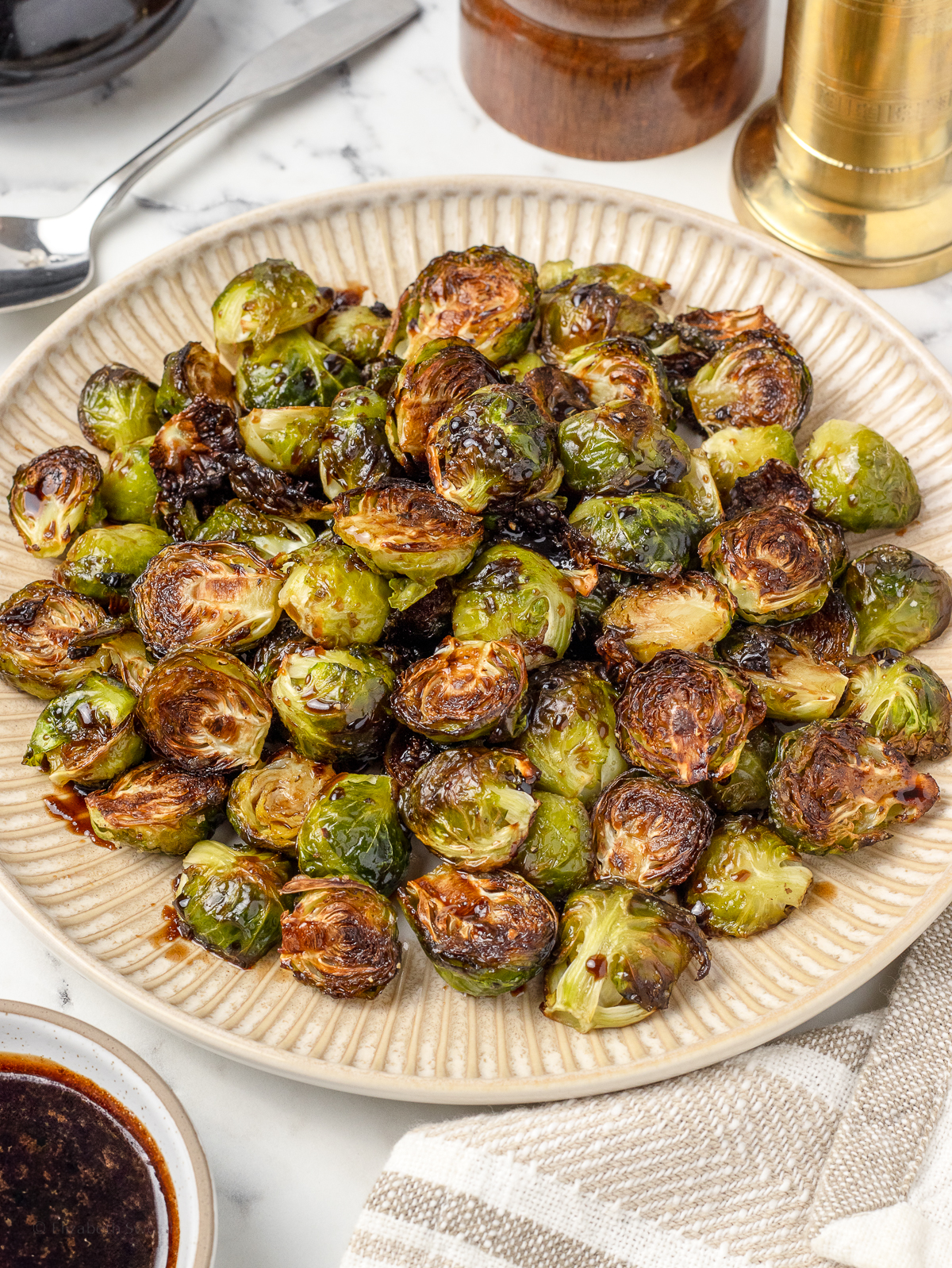 A large platter of roasted brussels sprouts glazed in a balsamic honey sauce. They are ready to serve with more glaze.