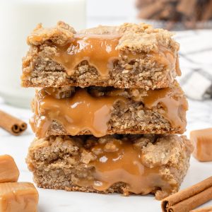 Stack of 3 gooey Caramel Bars. They are oozing caramel and surrounded by cinnamon oat crumble layers.