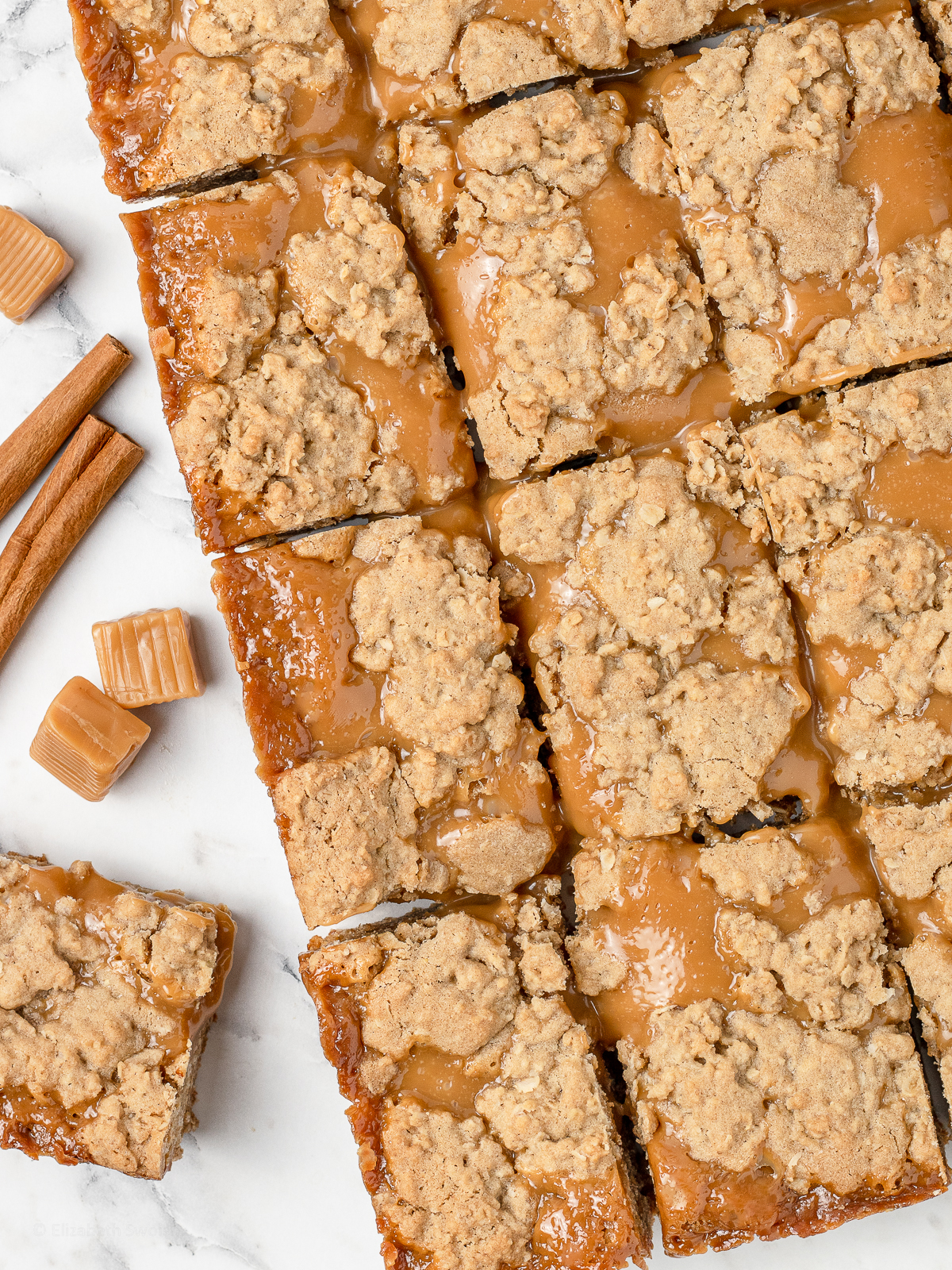 Overhead shot of slices of Caramel Bars with cinnamon sticks and caramel squares on the side.