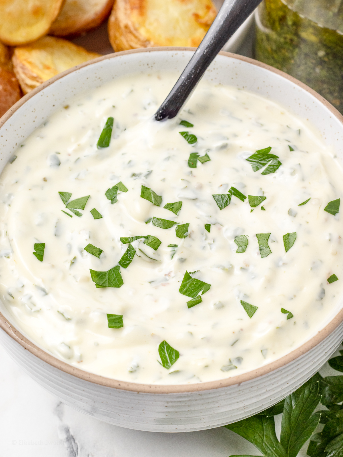 Close up of the aioli to see flecks of parsley and chimichurri. It is a thick and creamy dipping sauce.