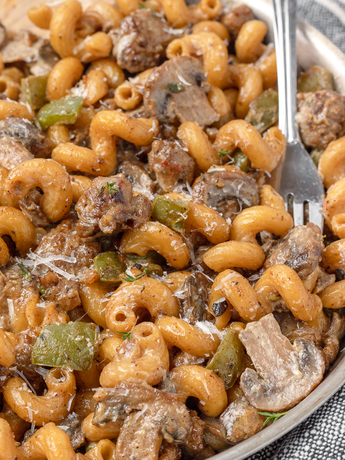 Pan of pasta with a fork in it. There's a creamy sauce covering pasta, mushrooms, Italian sausage, and green peppers.