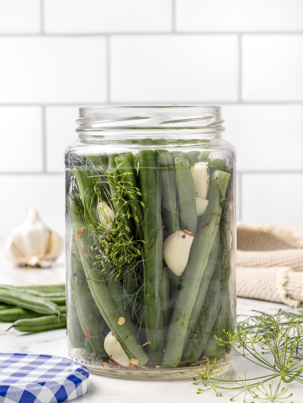 Jars packed with snipped green beans, halved garlic cloves, fresh dill, and red pepper flakes.