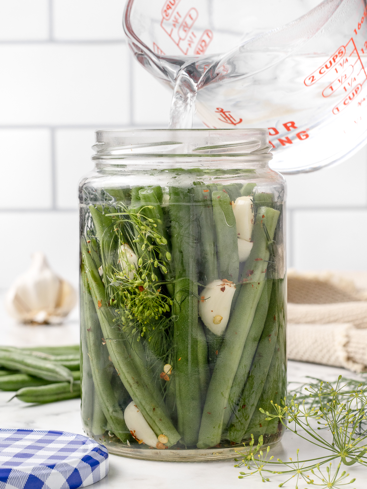 Pouring the warmed vinegar, water, and salt brine over the jar of green beans.